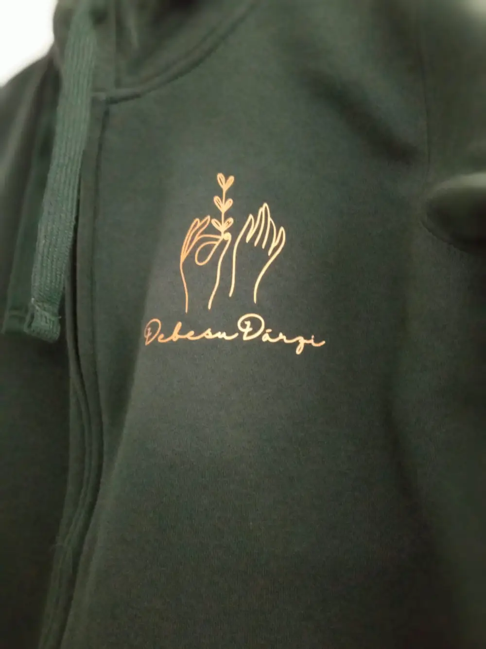 Green hooded jacket with a gold Debesu Dārzi logo on the chest