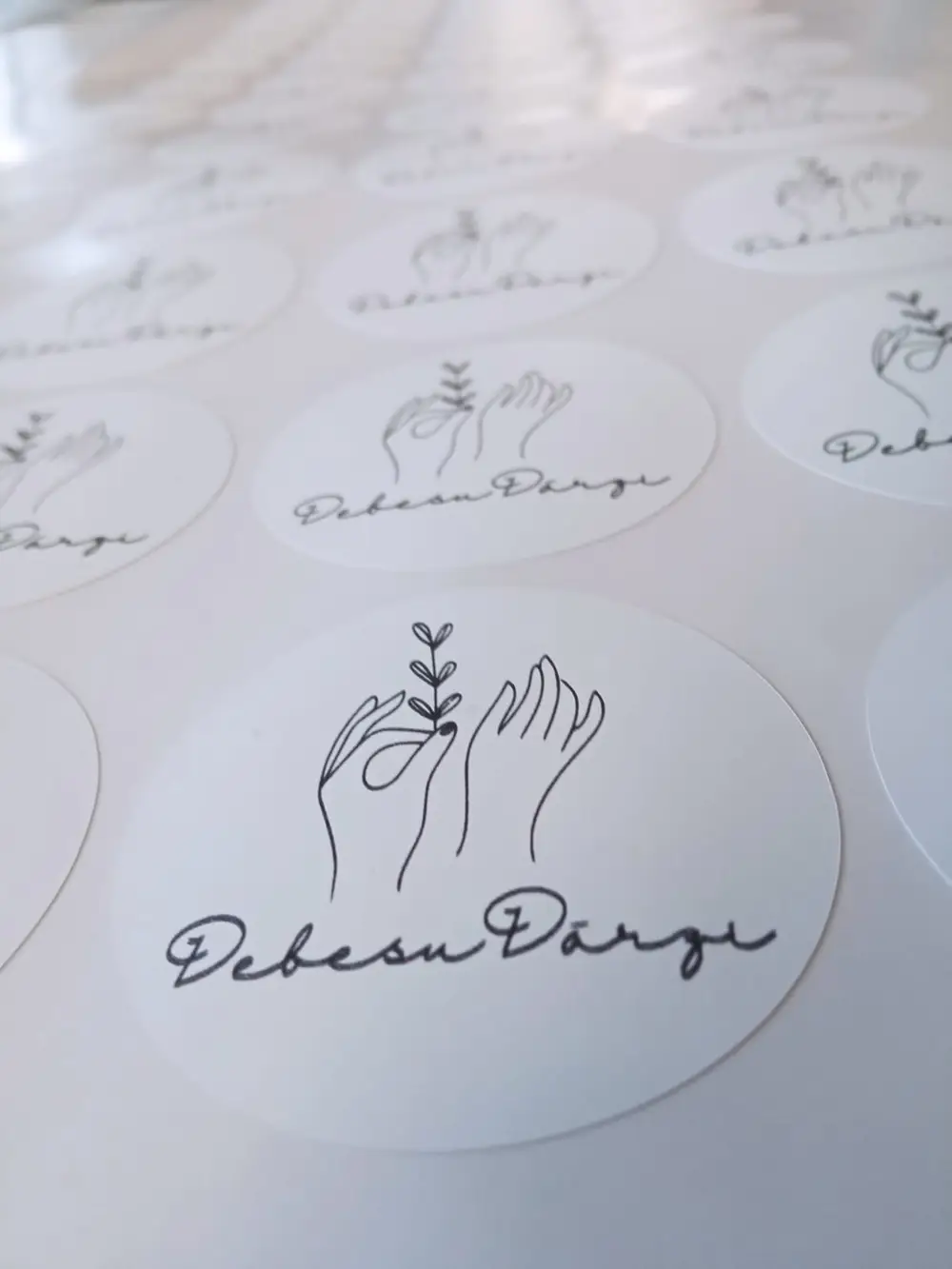 White round stickers with the hand-drawn Debesu Dārzi logo on a sheet