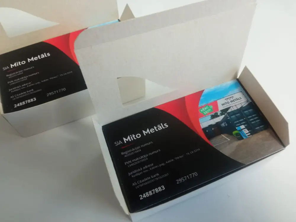 Black and red SIA Mito Metāls business cards in an open cardboard box