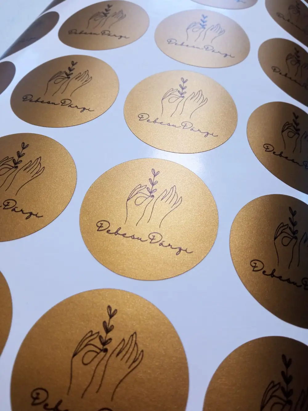 Round gold stickers with a black Debesu Dārzi logo