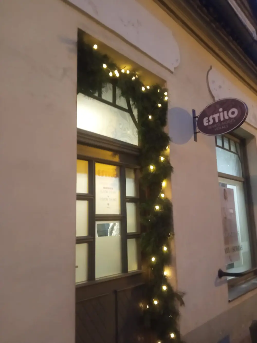 Oval projecting sign for the Estilo women’s fashion shop on a facade in the evening