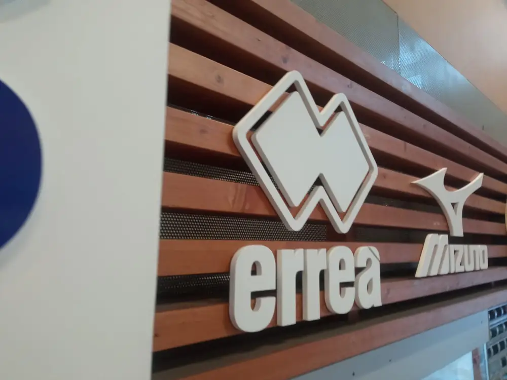 White 3D errea and Mizuno logos on a wooden slat wall