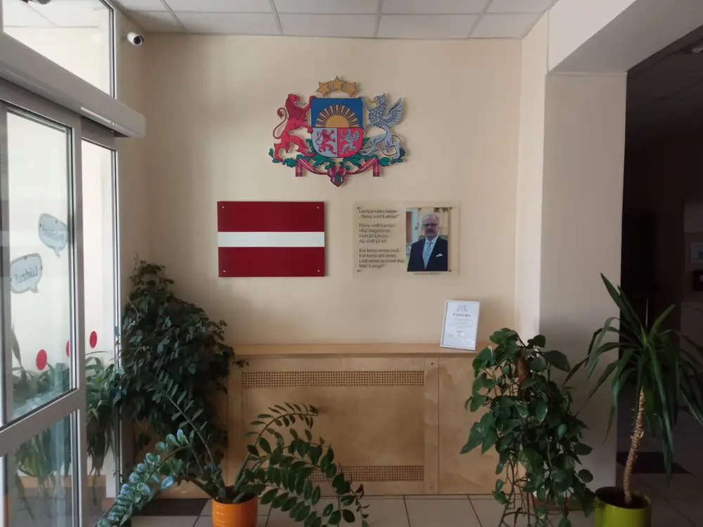 Latvian coat of arms, a flag plaque and a plaque with the anthem text and a portrait on a wall