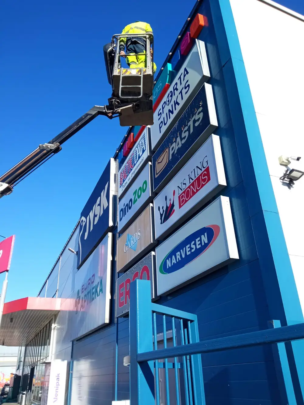 Installer on a lift at a facade board with signs for several shops