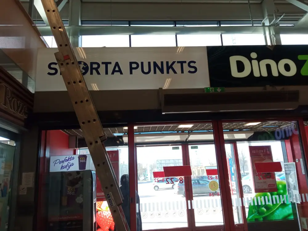 Shopping centre entrance with Sporta Punkts and Dino Zoo signs, a ladder by the wall