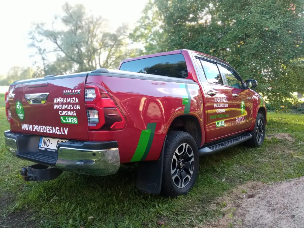 Red pickup truck with green stripes and the text priedesag.lv