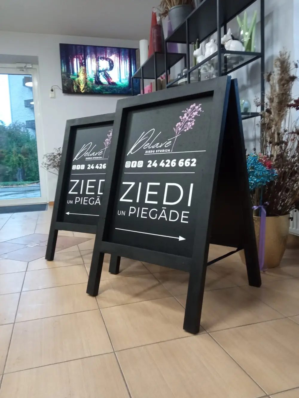 Two black pavement signs reading Delavé ziedu studija, Ziedi and piegāde