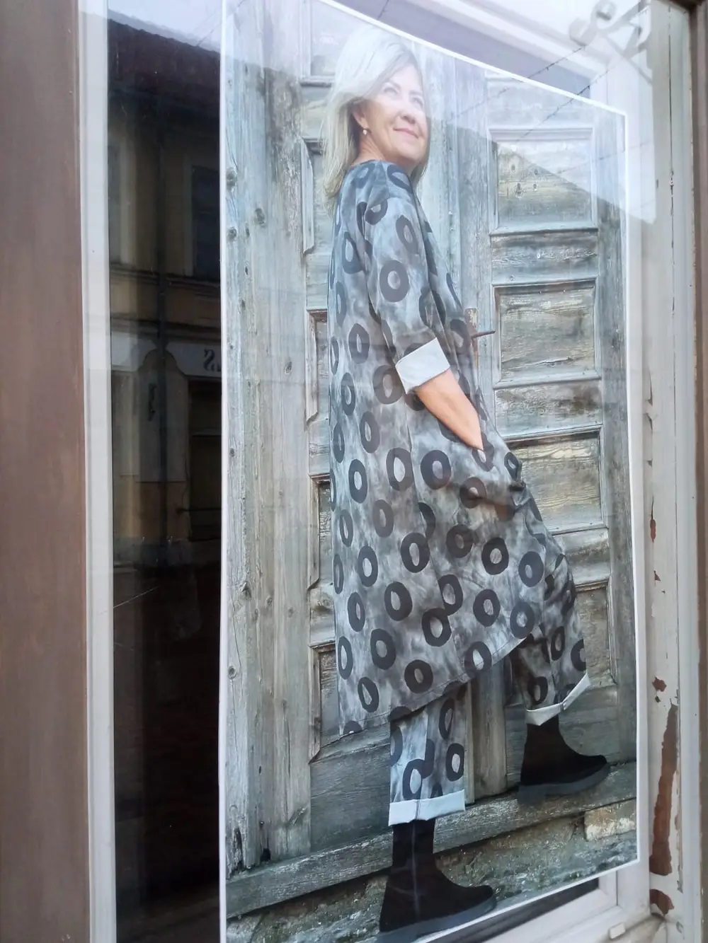 Shop window poster of a woman in a patterned outfit by a wooden door