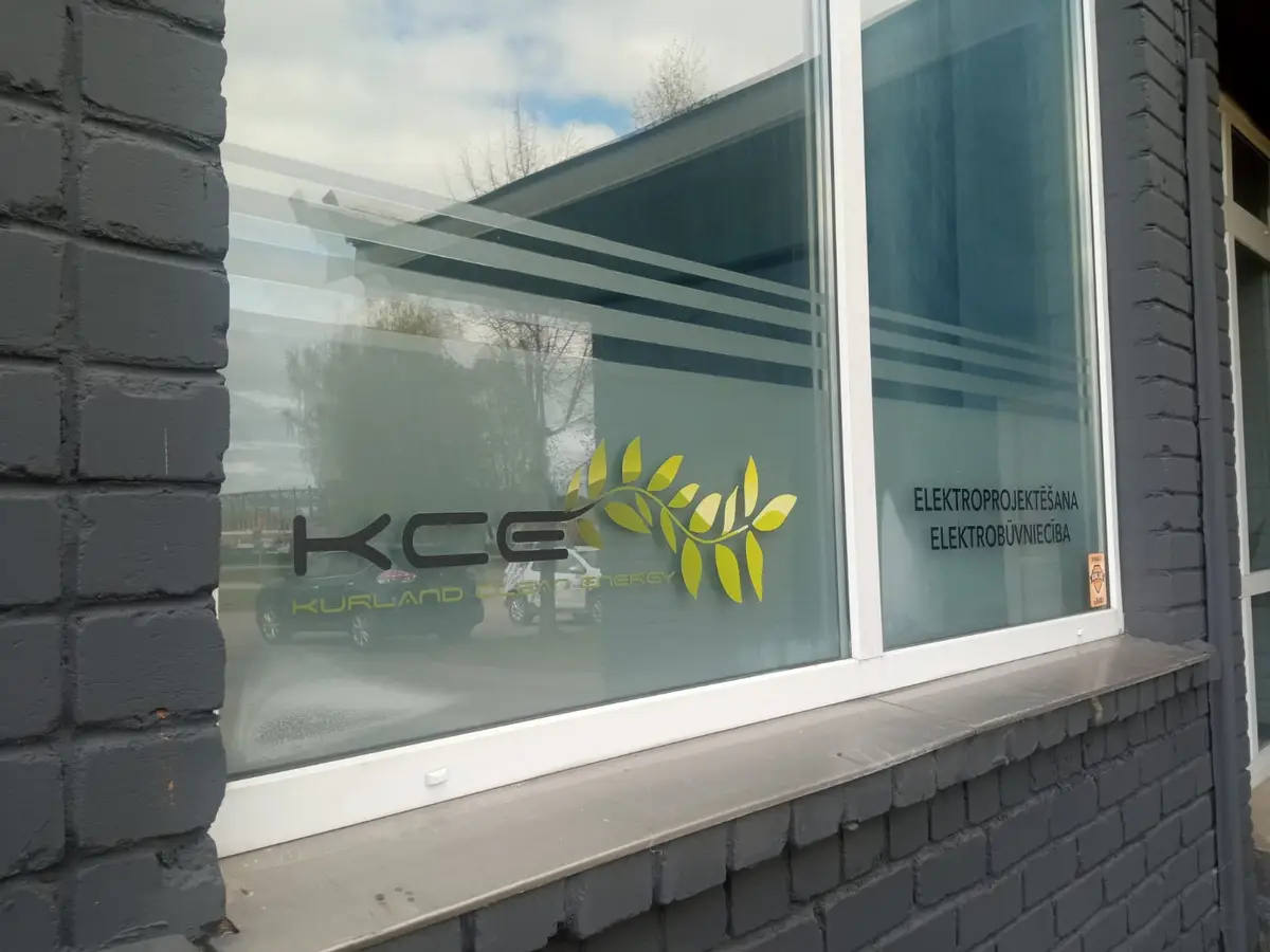 Office window with frosted film stripes, the KCE logo with yellow leafy branches and lettering about electrical design