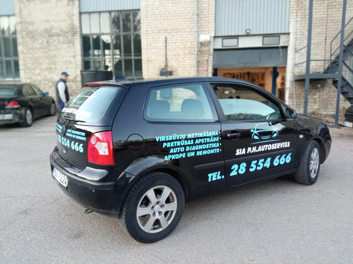 Black VW Polo with light blue lettering about car service work and a phone number on the side