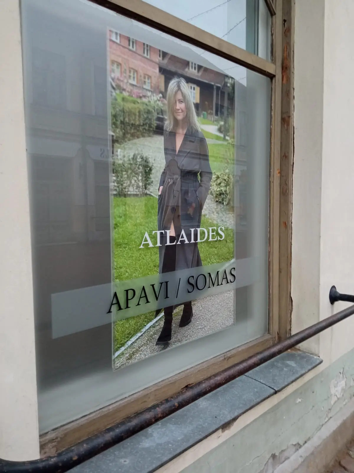 Shop window with frosted glass, a poster of a woman in a coat and the text "Atlaides, apavi / somas"